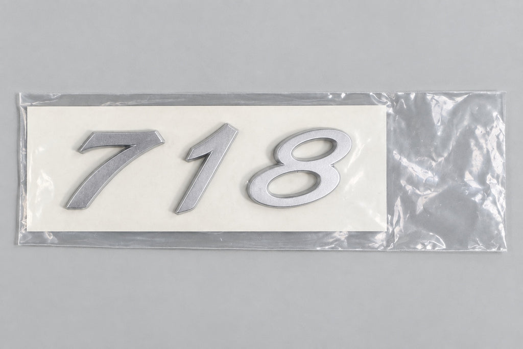 Silver-coloured aftermarket 718 badge set in protective packaging
