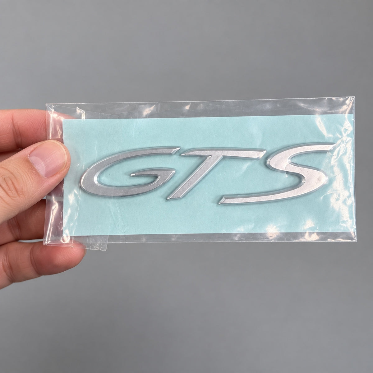 Silver-coloured aftermarket GTS badge set in protective packaging