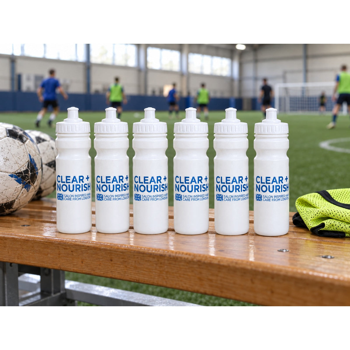 Six bottles on a sports hall bench, five-a-side match behind