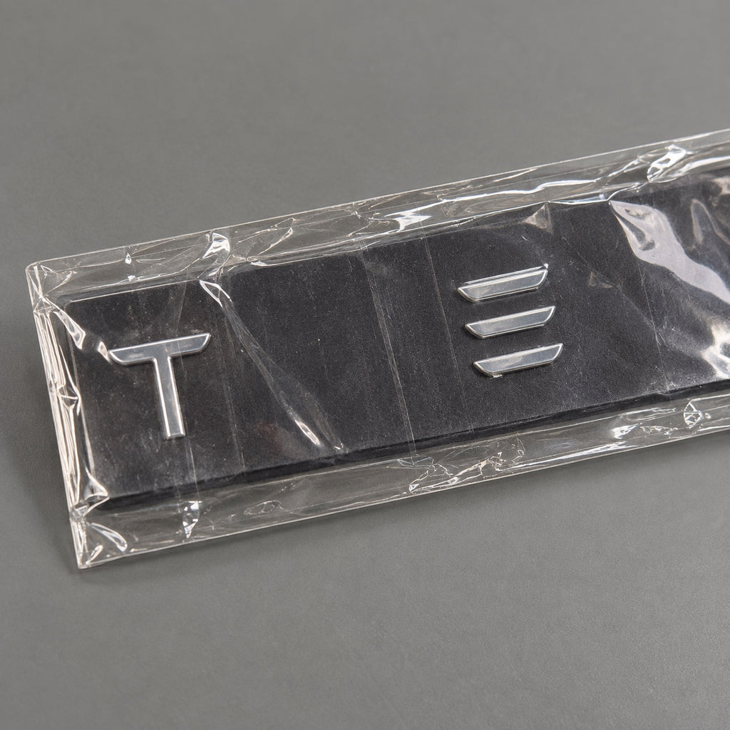 Silver-coloured aftermarket Tesla lettering set in protective packaging