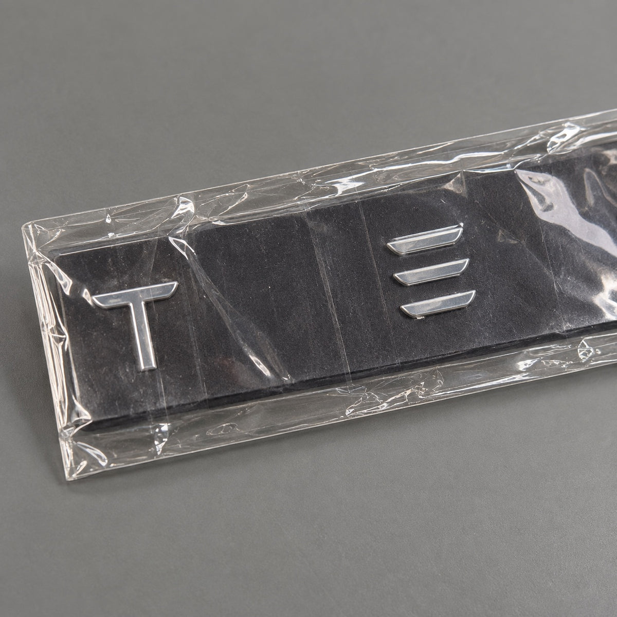 Silver-coloured aftermarket Tesla lettering set in protective packaging