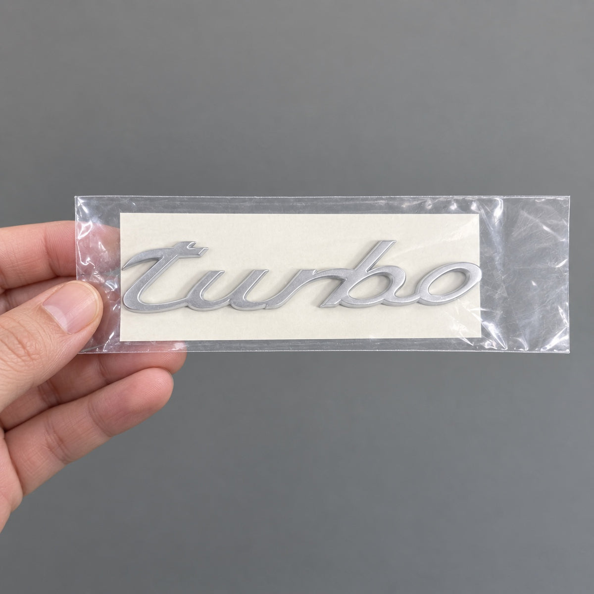 Silver-coloured aftermarket turbo script badge in protective packaging